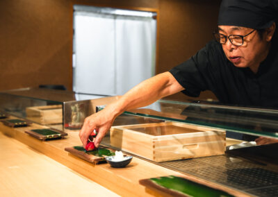 Chef placing a piece of tuna nigiri onto a wooden sushi board at Sushi Shutatsu.
