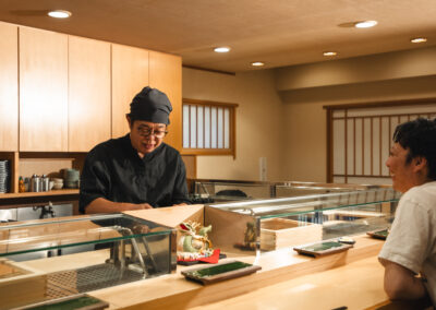Sushi chef interacting with a guest at the counter inside Sushi Shutatsu in Tokyo